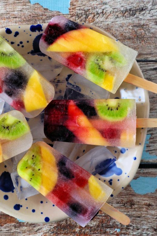 Healthy mixed fruit summer ice pops. Top view in bowl against a rustic blue wood background.