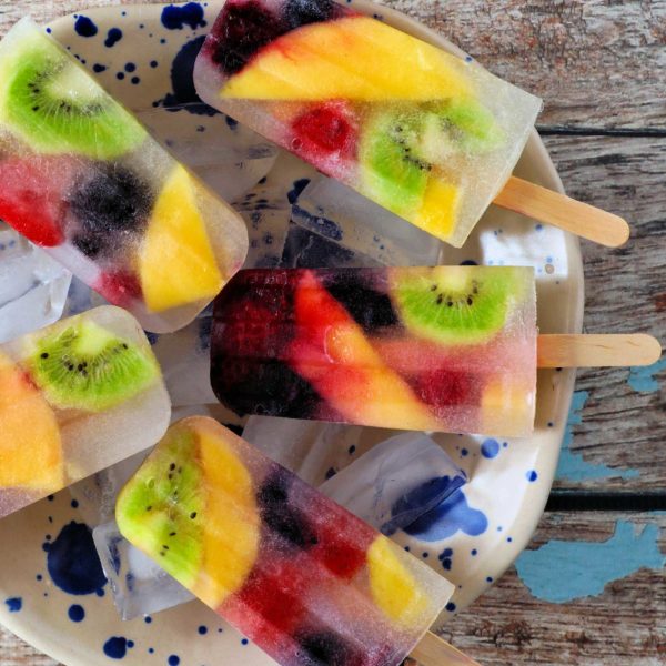 Healthy mixed fruit summer ice pops. Top view in bowl against a rustic blue wood background.